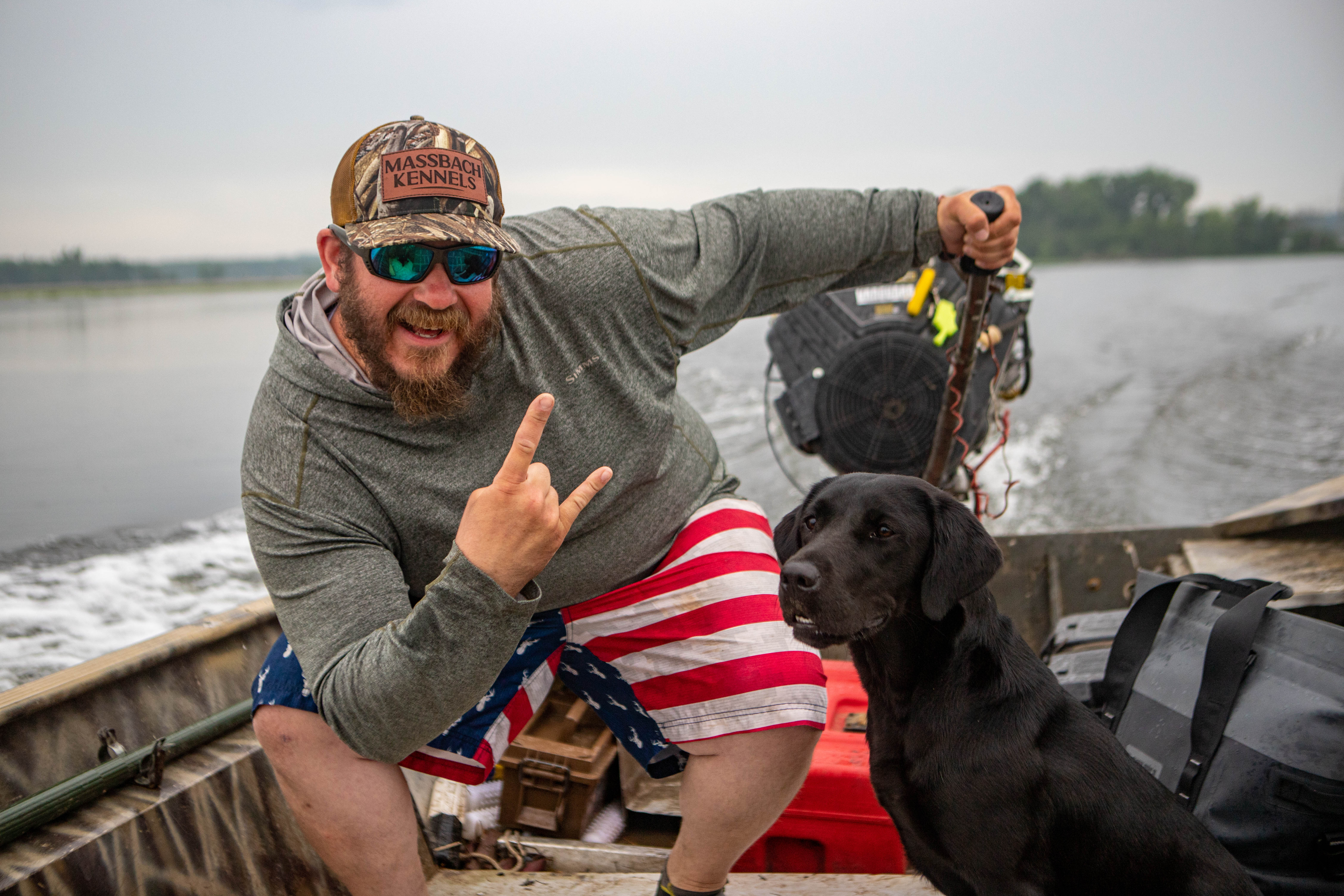Trainer with a black Labrador on a boat with hunting gear
